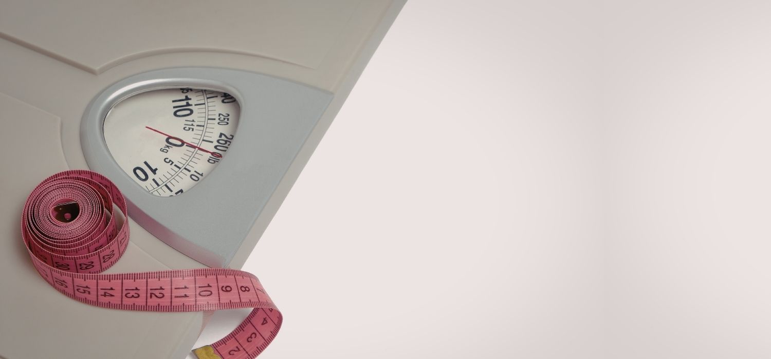 A bathroom scale and a pink measuring tape set against a clean, light background.