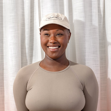 A woman smiling in a beige cap and top, embodying Happy V's wellness ethos.