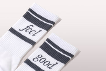 White socks featuring "feel good" text and black stripes, embodying Happy V's wellness ethos.