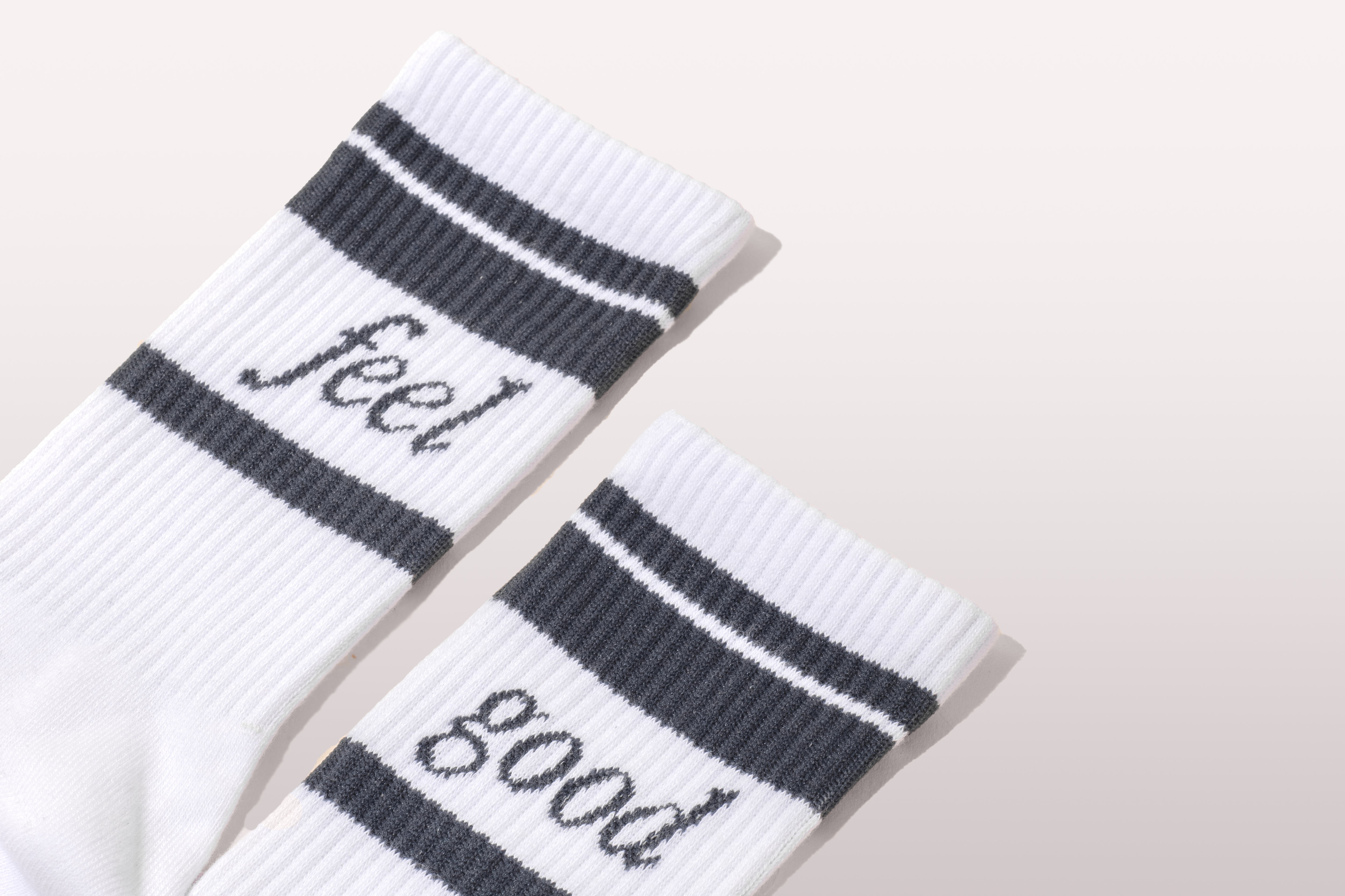 White socks featuring "feel good" text and black stripes, embodying Happy V's wellness ethos.