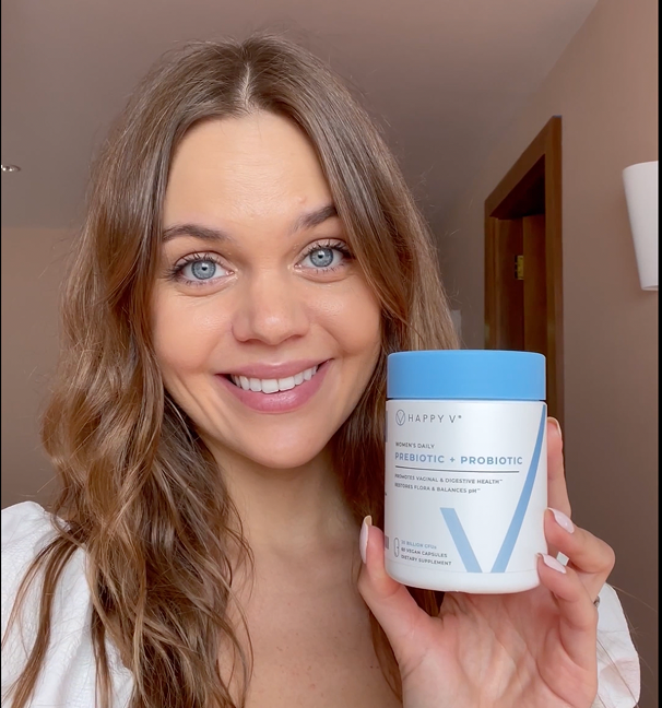 Woman holding a jar of Happy V Women's Daily Prebiotic + Probiotic in a well-lit indoor setting.