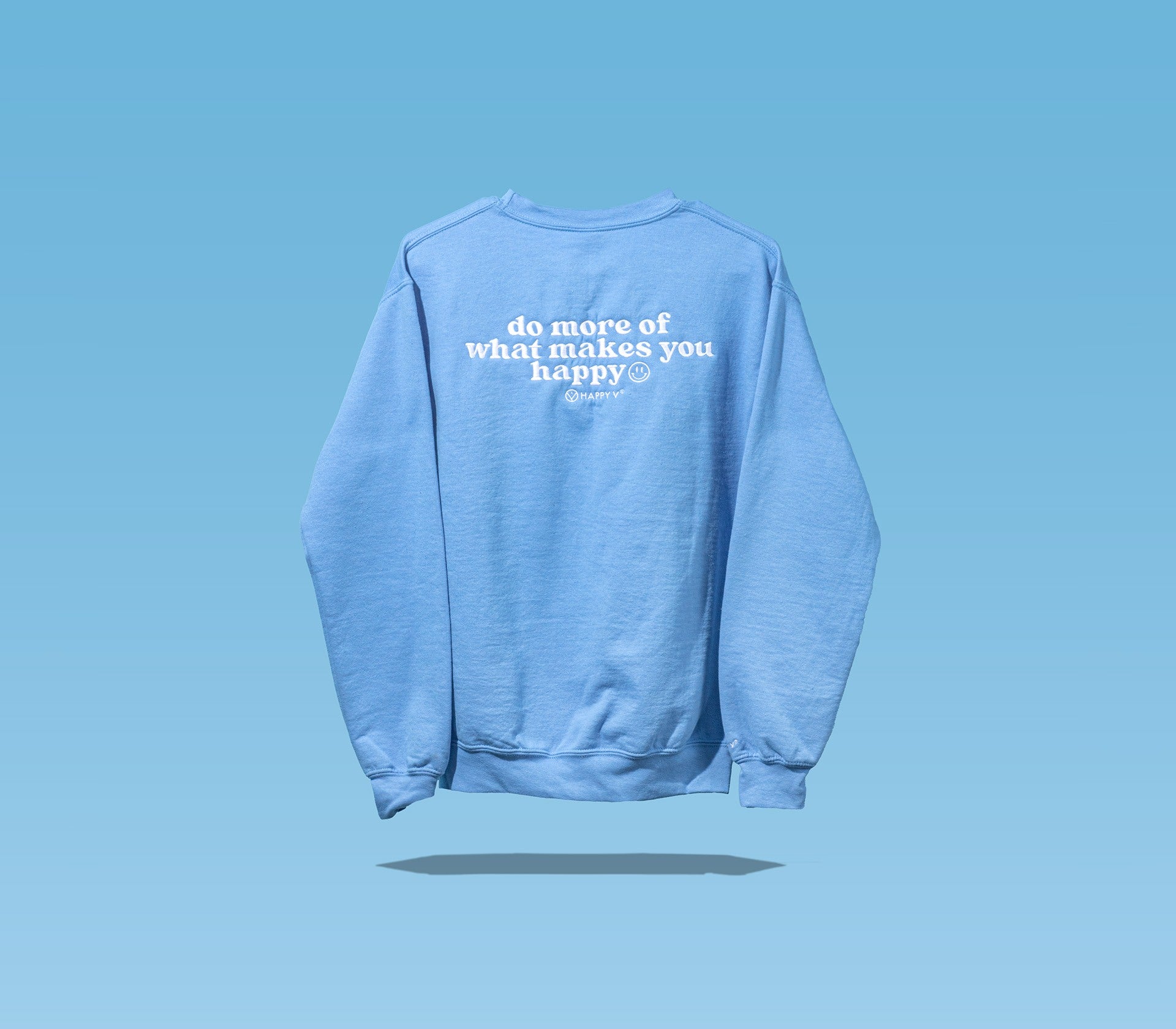 The back side of a Happy V Crewneck Sweatshirt in blue with a sentence on the shirt saying "do more of what makes you happy" against a blue background.