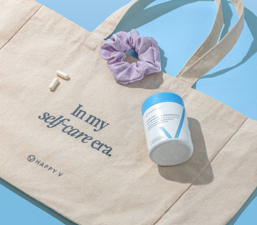 Flattened Happy V Tote Bag with a scrunchie and a bottle with supplements on top.