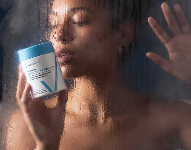Woman holding Happy V probiotic supplement against a foggy glass background.