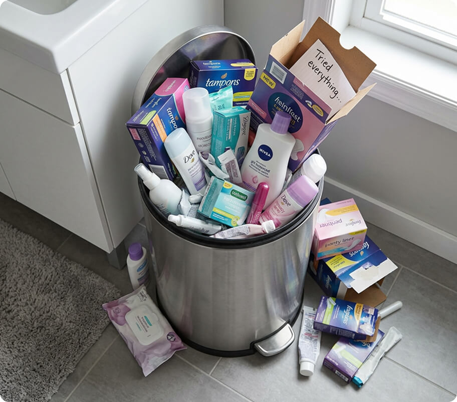 A trash can overflowing with empty health product boxes and bottles related to women's wellness.